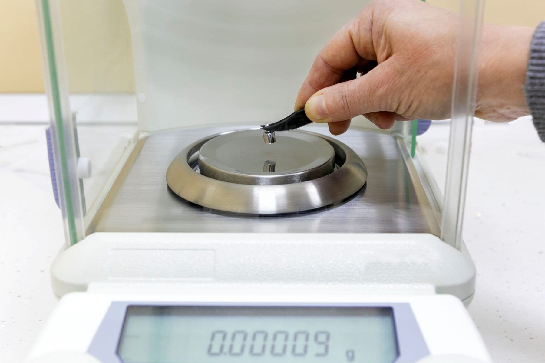 Tweezers placing a small weight on an analytical balance