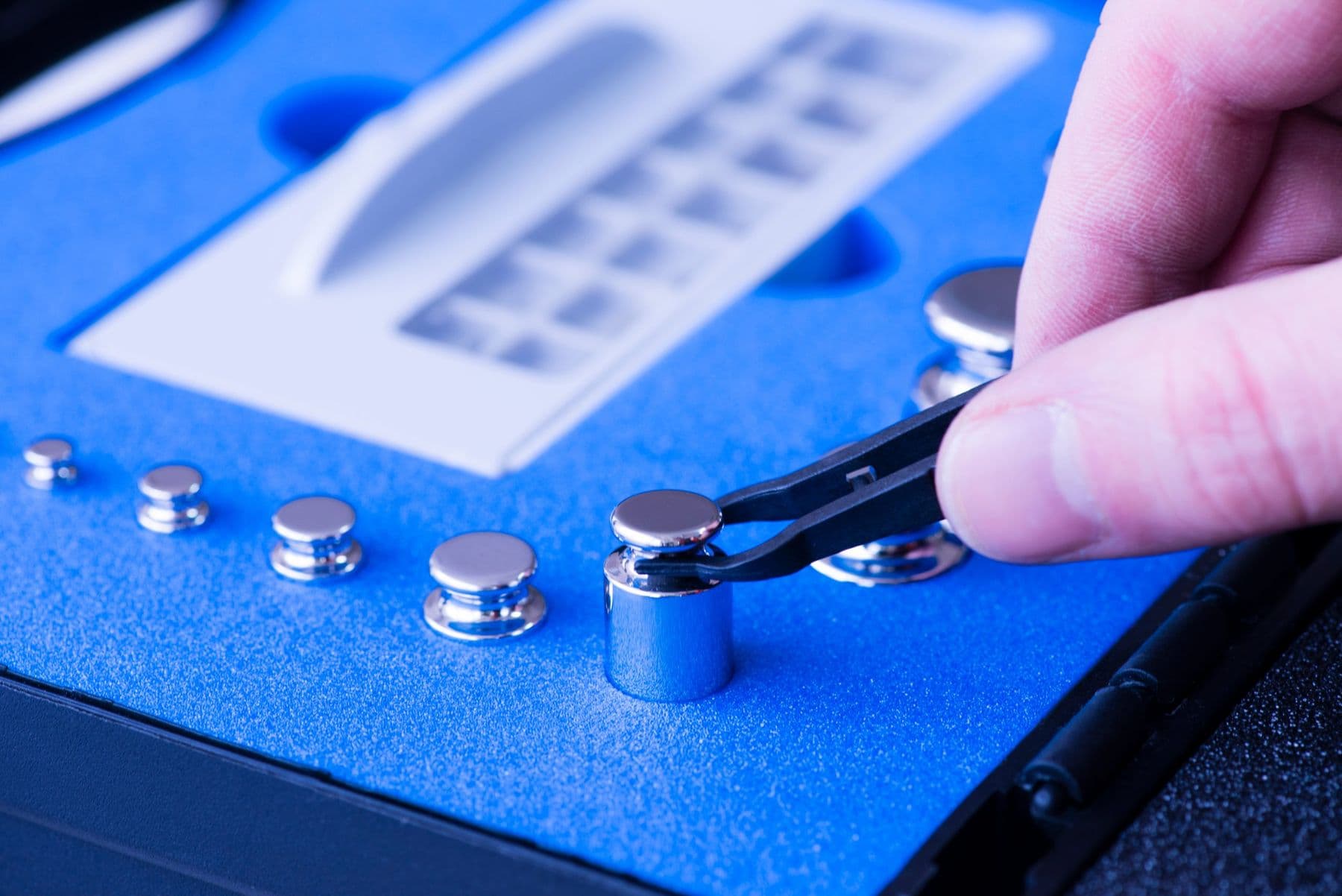Tweezers selecting a calibration weight from a foam-lined case